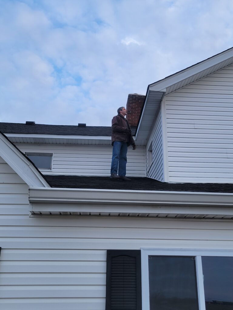 JD Taggart on the roof inspecting gutters, shingles and chimney.
